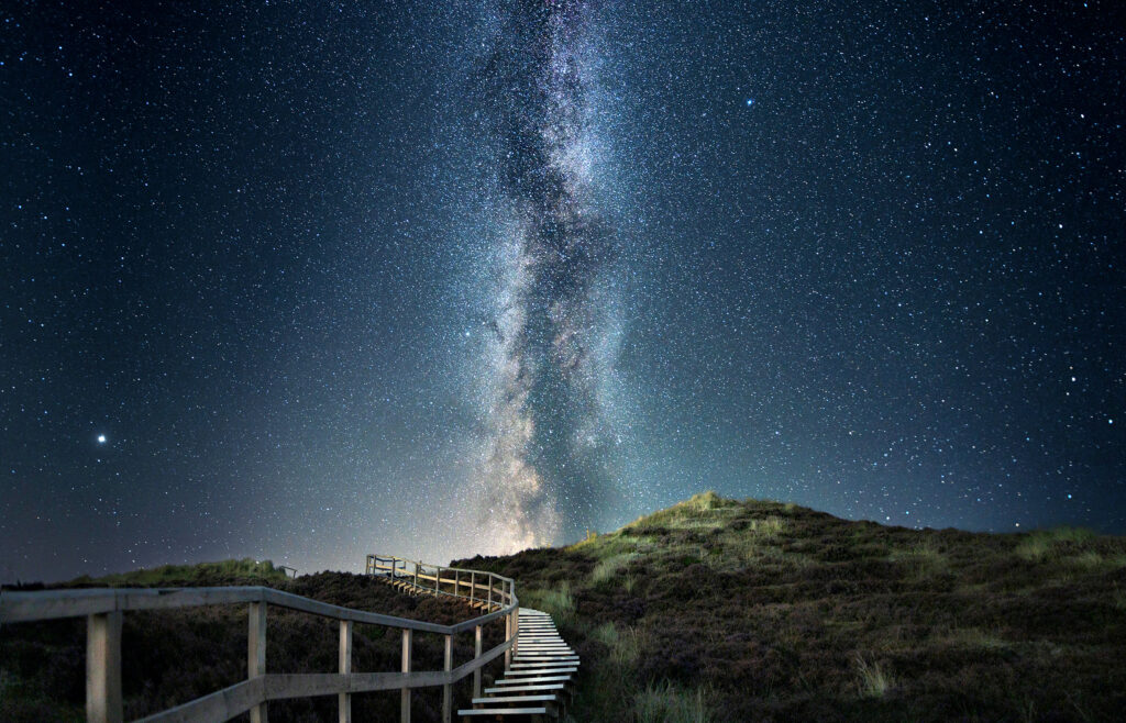 Holzsteg in den Kampener Dünen unter der Milchstraße bei Nacht.